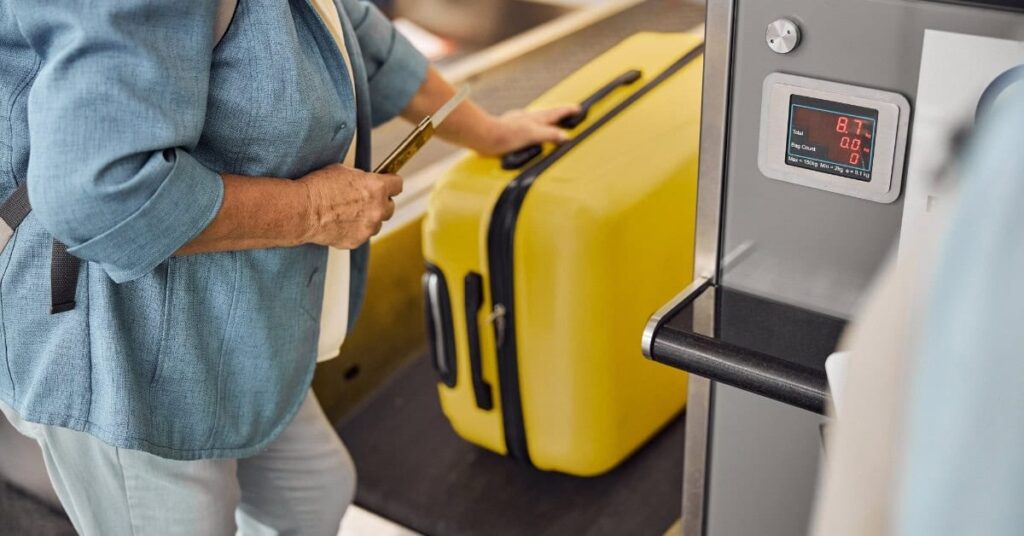 Passagier wiegt Koffer am Check-in-Schalter des Flughafens Bali – Vorbereitung auf die automatische Gepäckkontrolle.